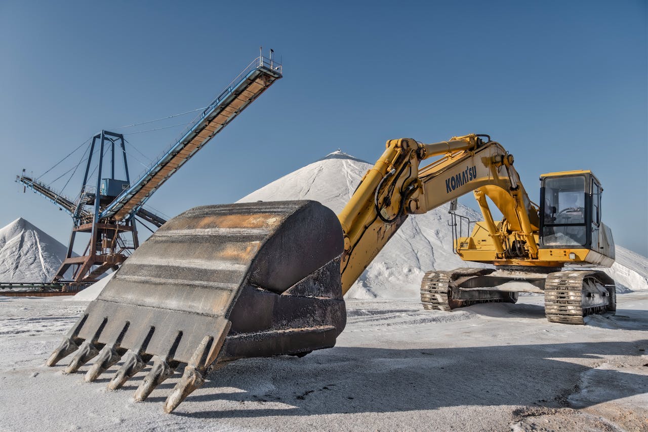 Excavator and conveyor system in a snowy quarry under clear skies.