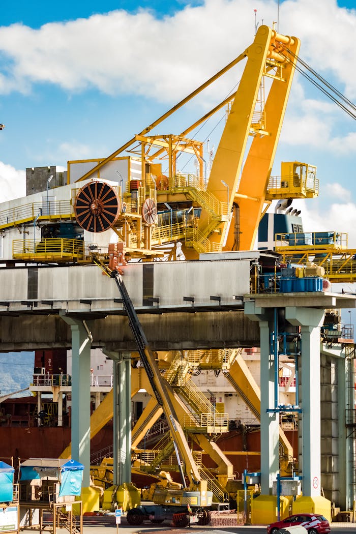 Close-up of a large industrial crane at a bustling shipyard harbor under a clear sky.